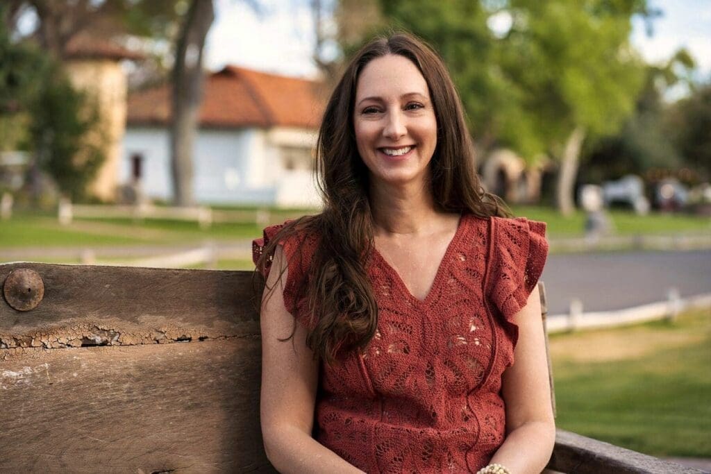 J sits near a rustic fence for a close portrait in her red blouse.