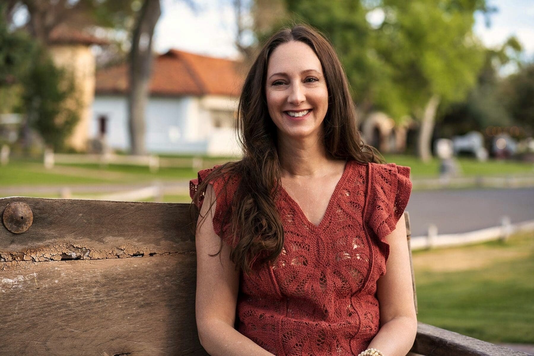 J sits near a rustic fence for a close portrait in her red blouse.
