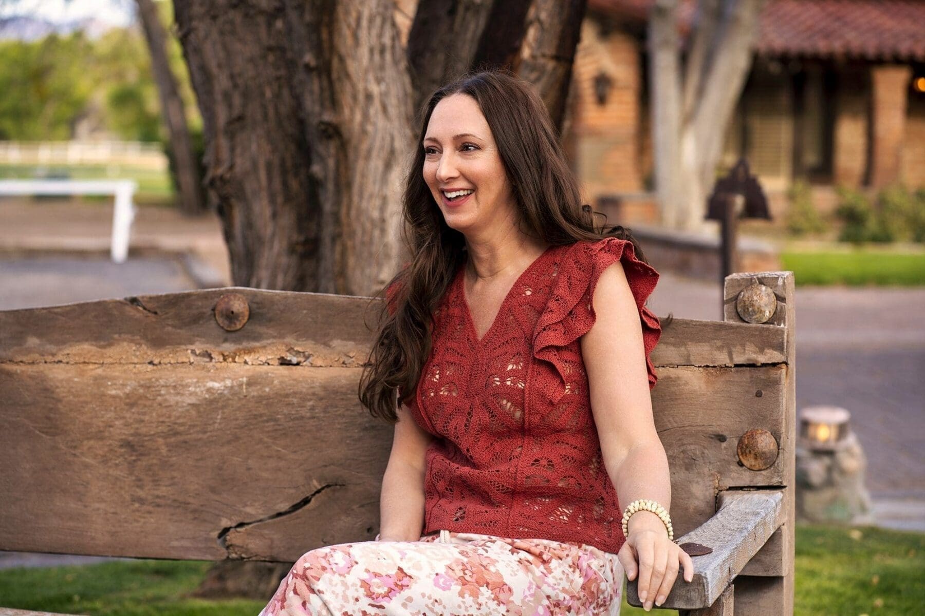 J sits on a rustic bench and laughs while looking to the side.