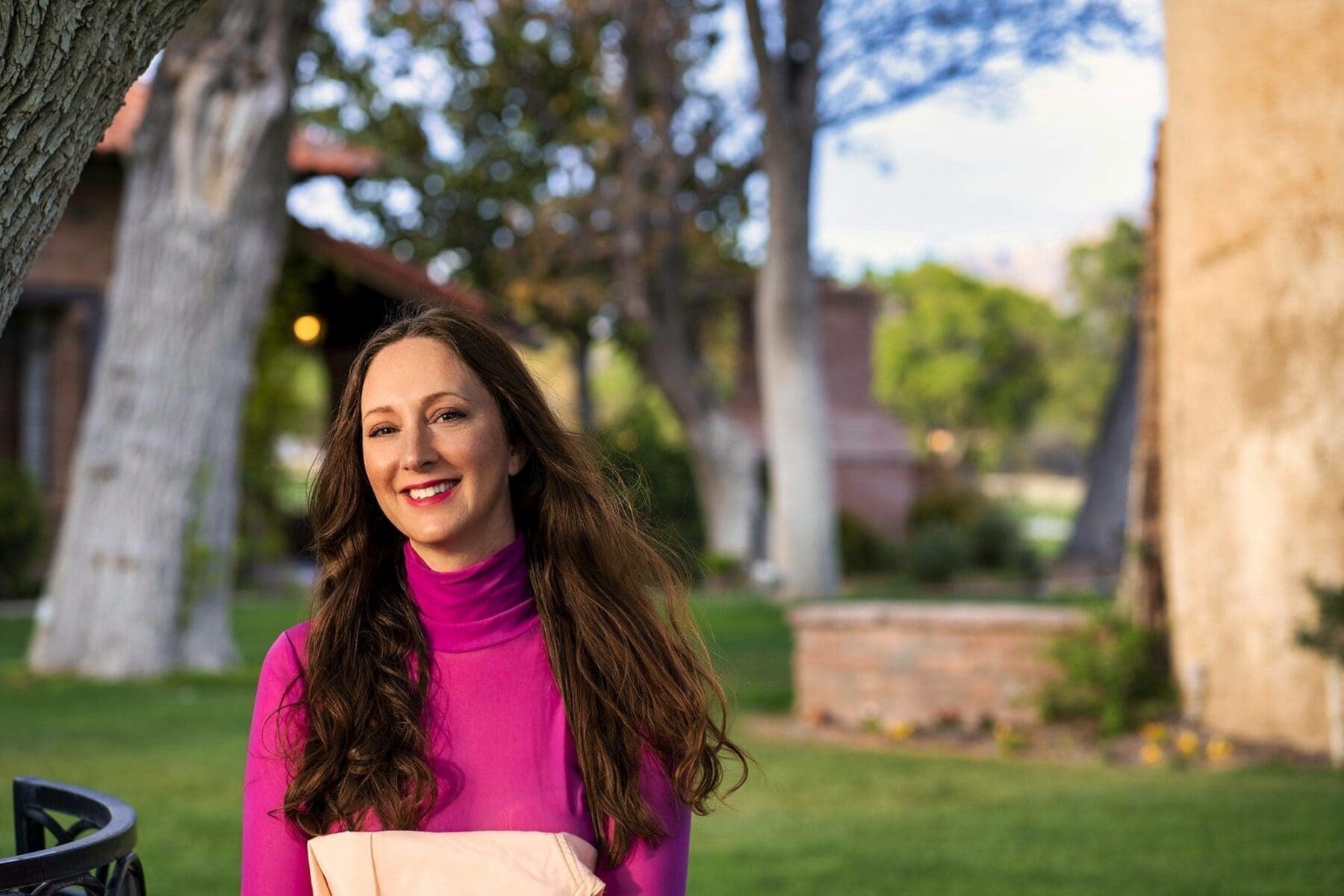 J faces the camera in a close outdoor portrait wearing a bright magenta top.