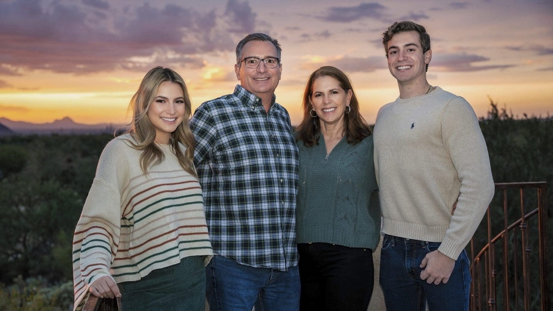 Four family members pose together on a terrace beneath layered pink clouds over the desert.