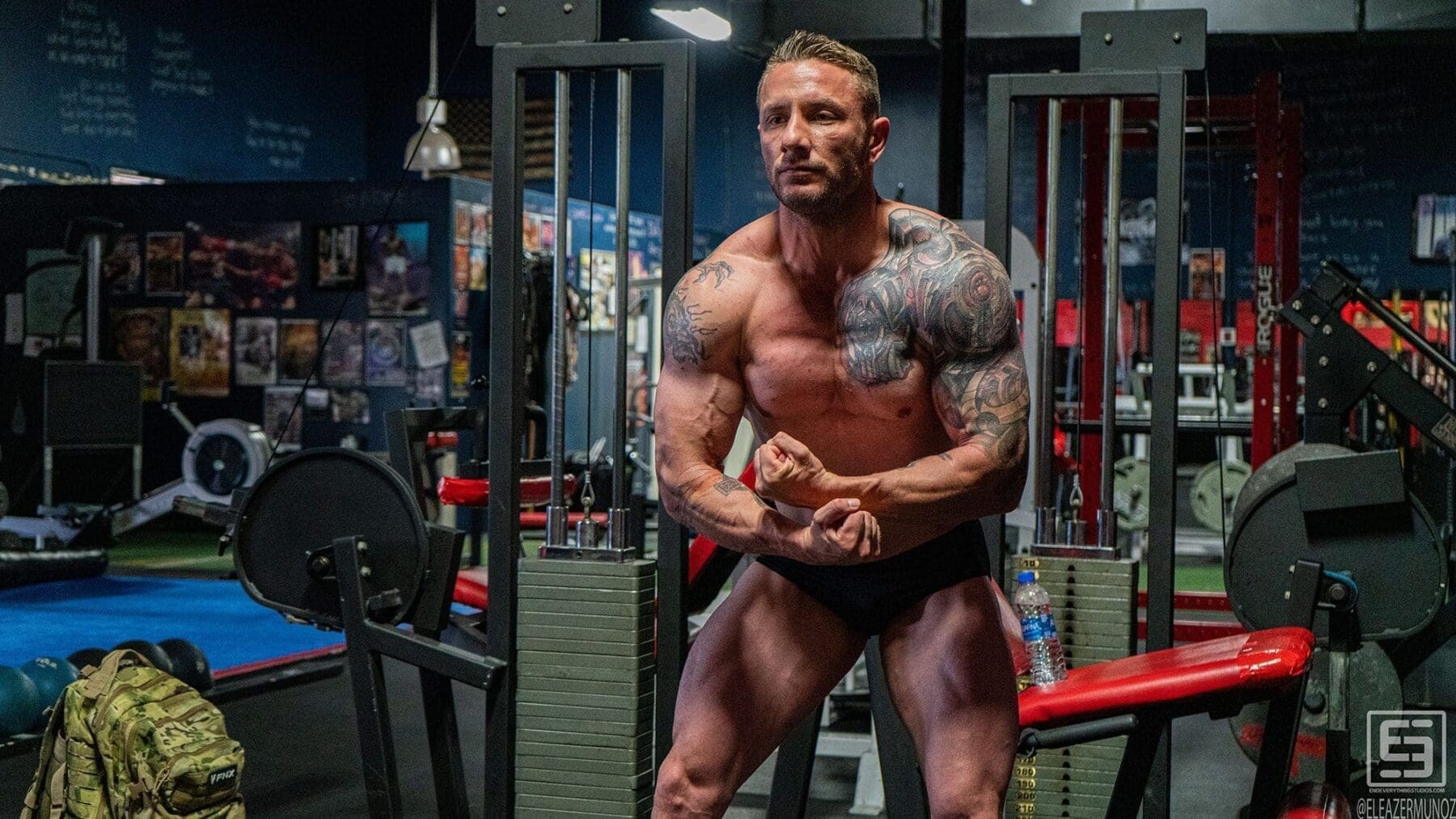 Irish Michael leans forward in a most-muscular pose between weight machines and a red bench.