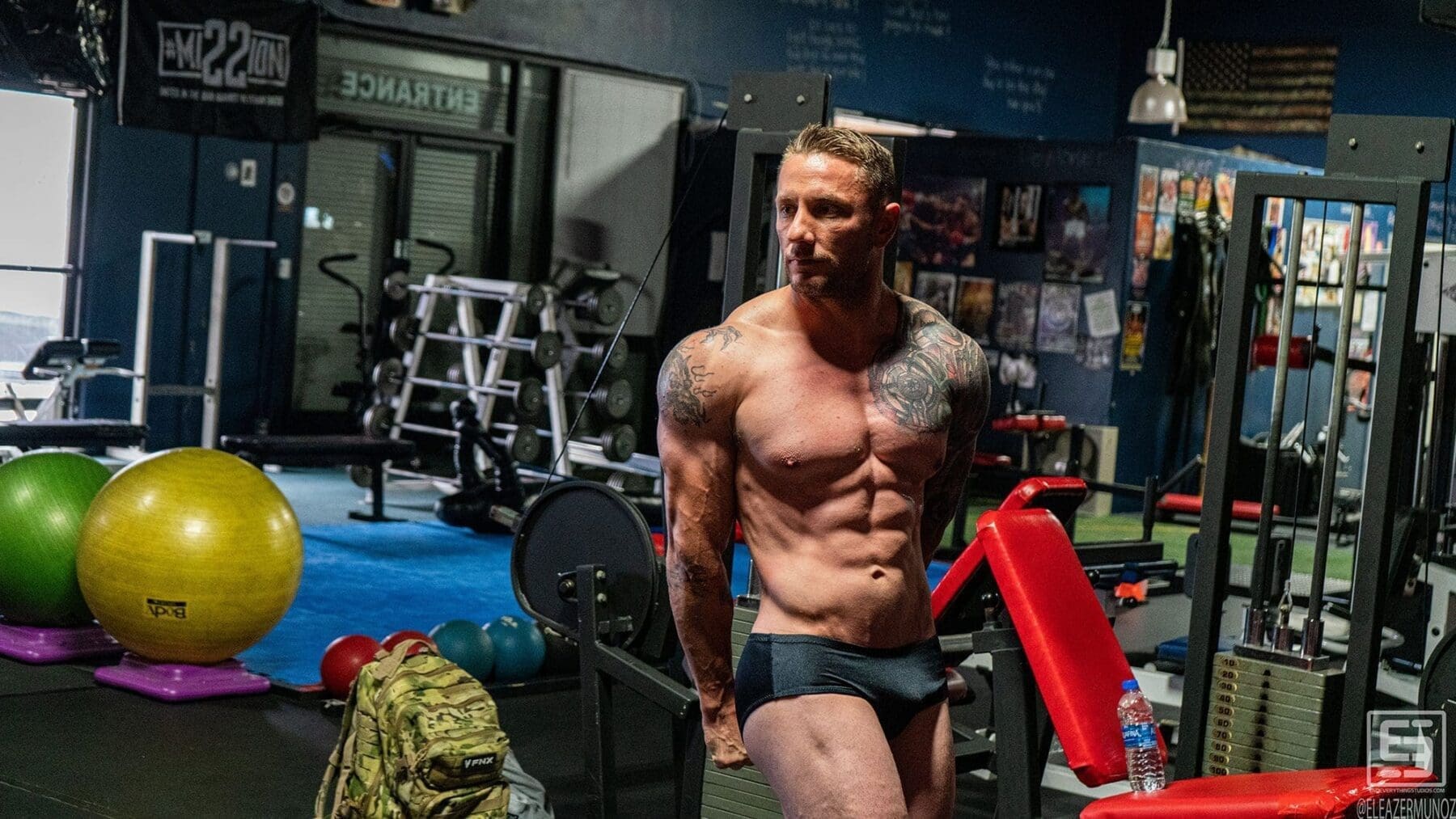 Irish Michael walks toward the camera through the gym with dramatic light across his torso.