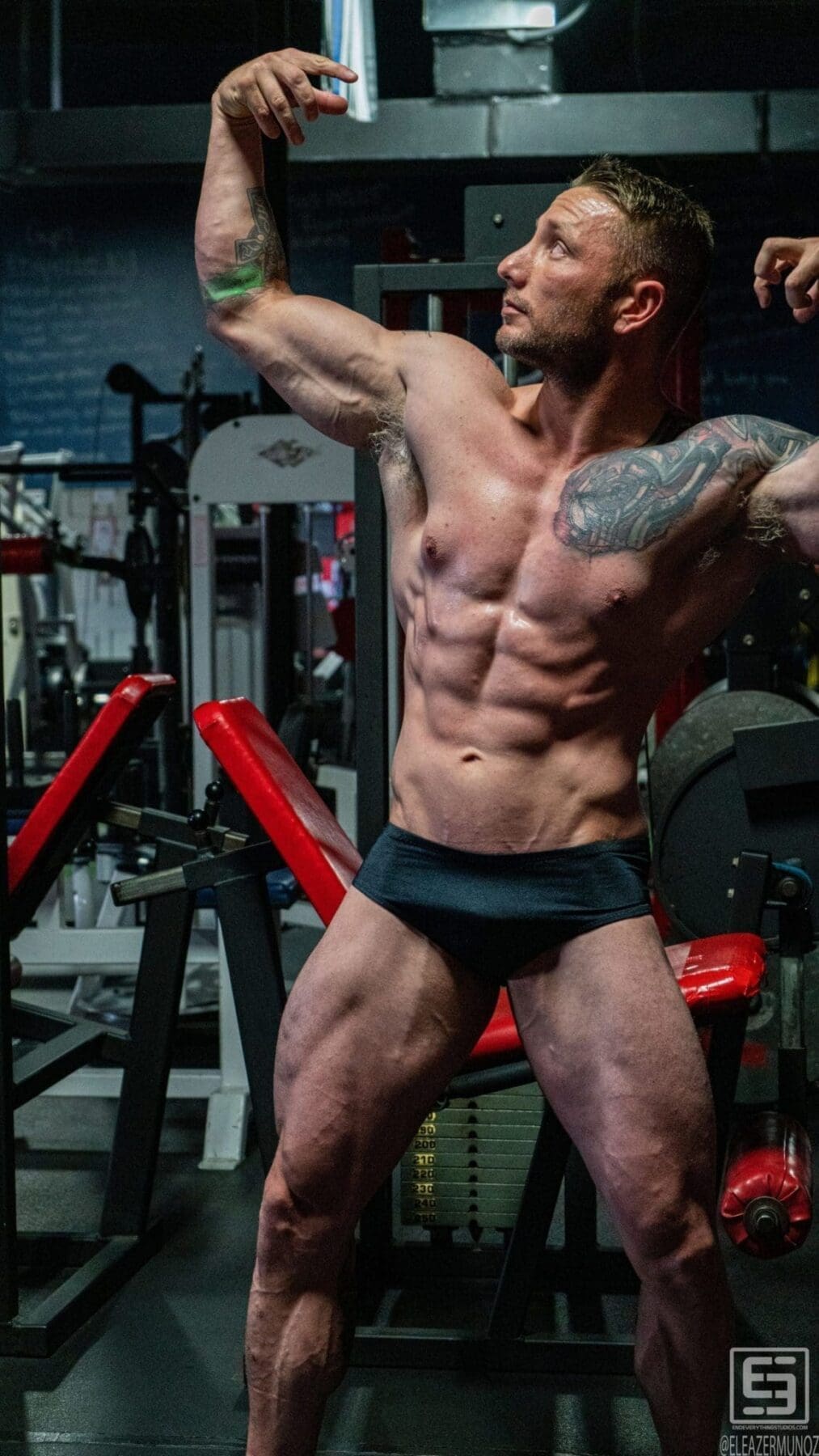 Irish Michael holds an overhead classic bodybuilding pose in a vertical full-body portrait.