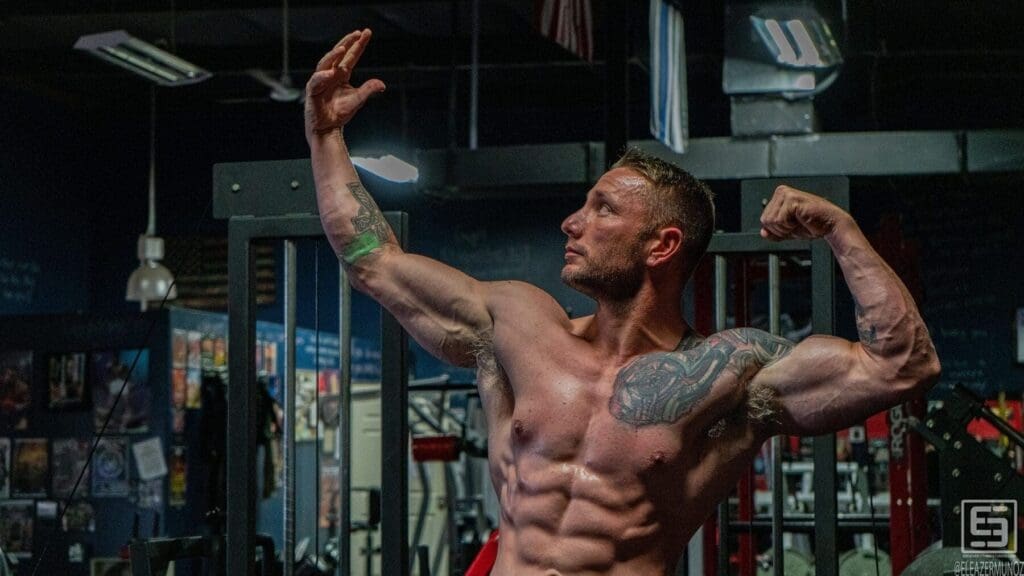 Irish Michael raises one arm and flexes the other in a close horizontal physique portrait.