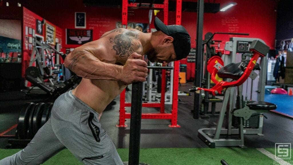 Irish Michael leans forcefully into the handles of a weighted sled during a close side view.