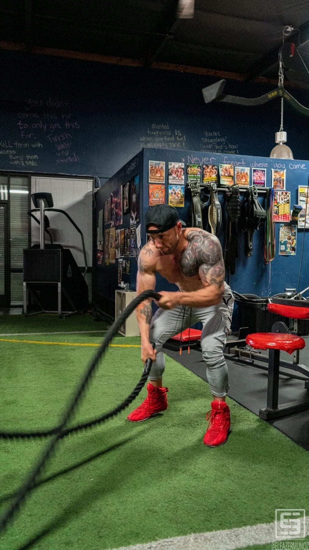 Irish Michael works heavy battle ropes on green turf while wearing gray pants and bright red shoes.